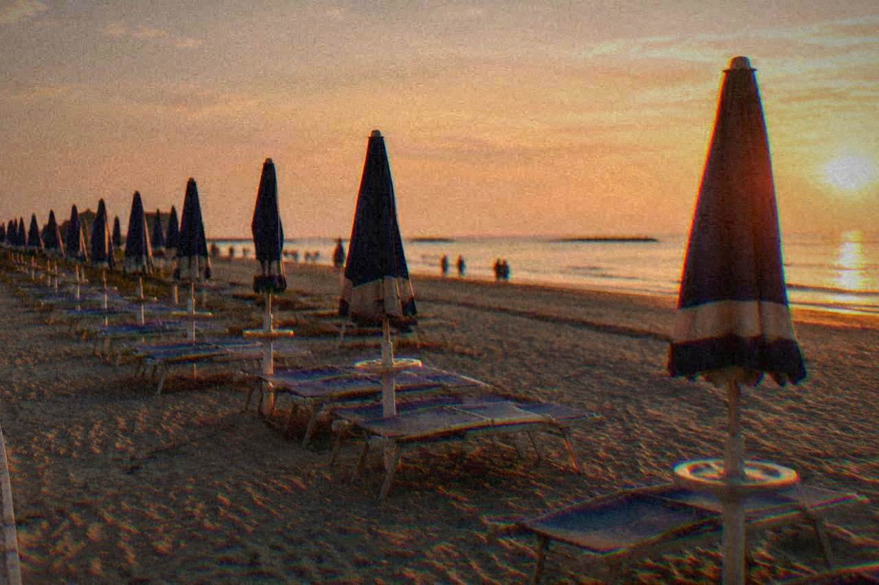 Rows of beach umbrellas on a wide sandy shore beside calm Adriatic water