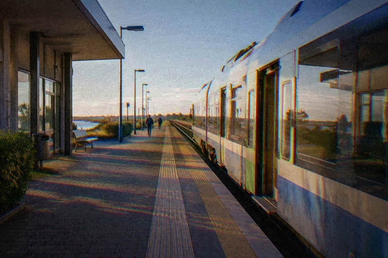 A regional train waiting at a platform beside a modern Italian railway station