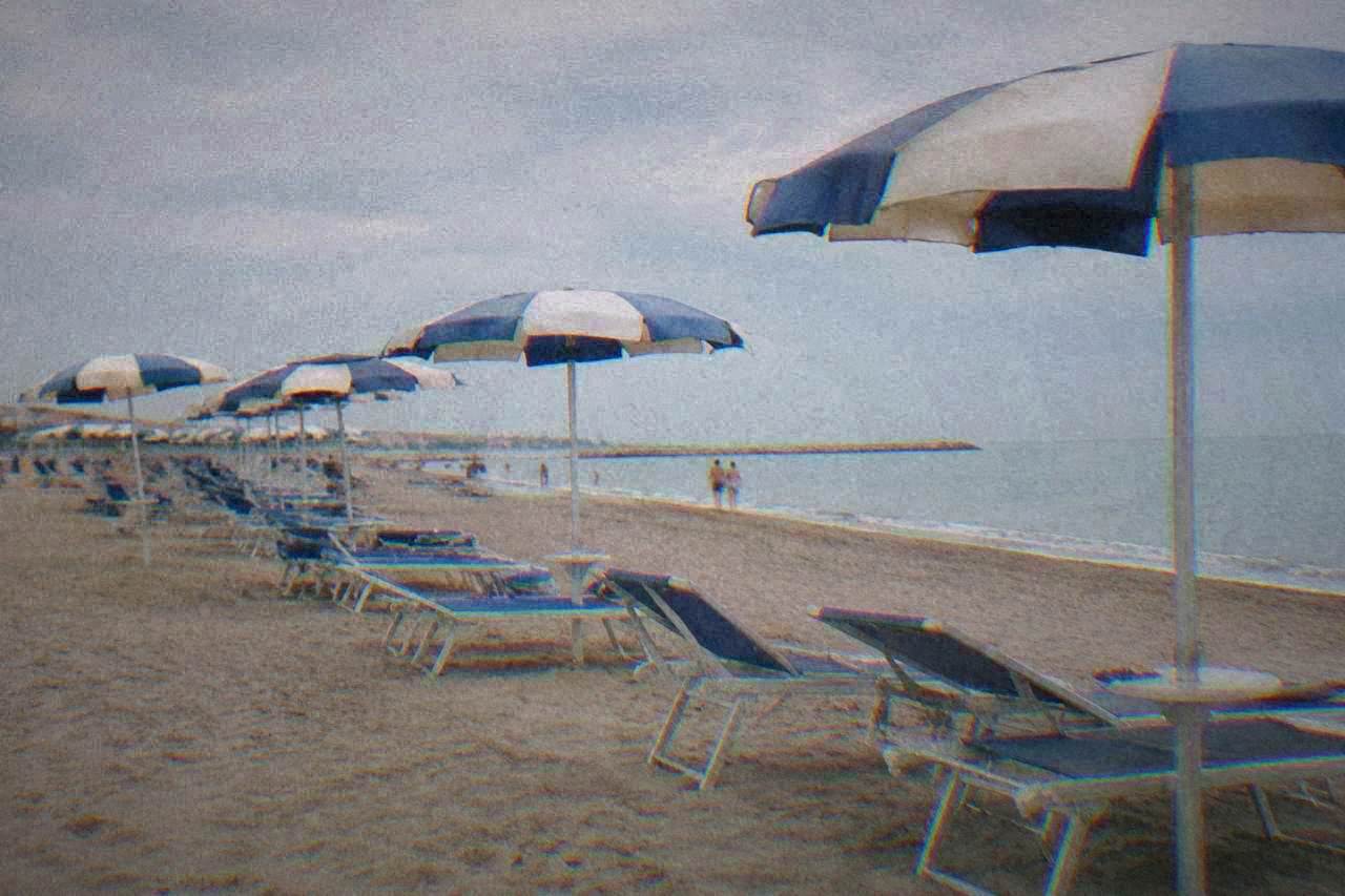 Rows of sun umbrellas on a wide sandy beach beside a calm Adriatic shoreline