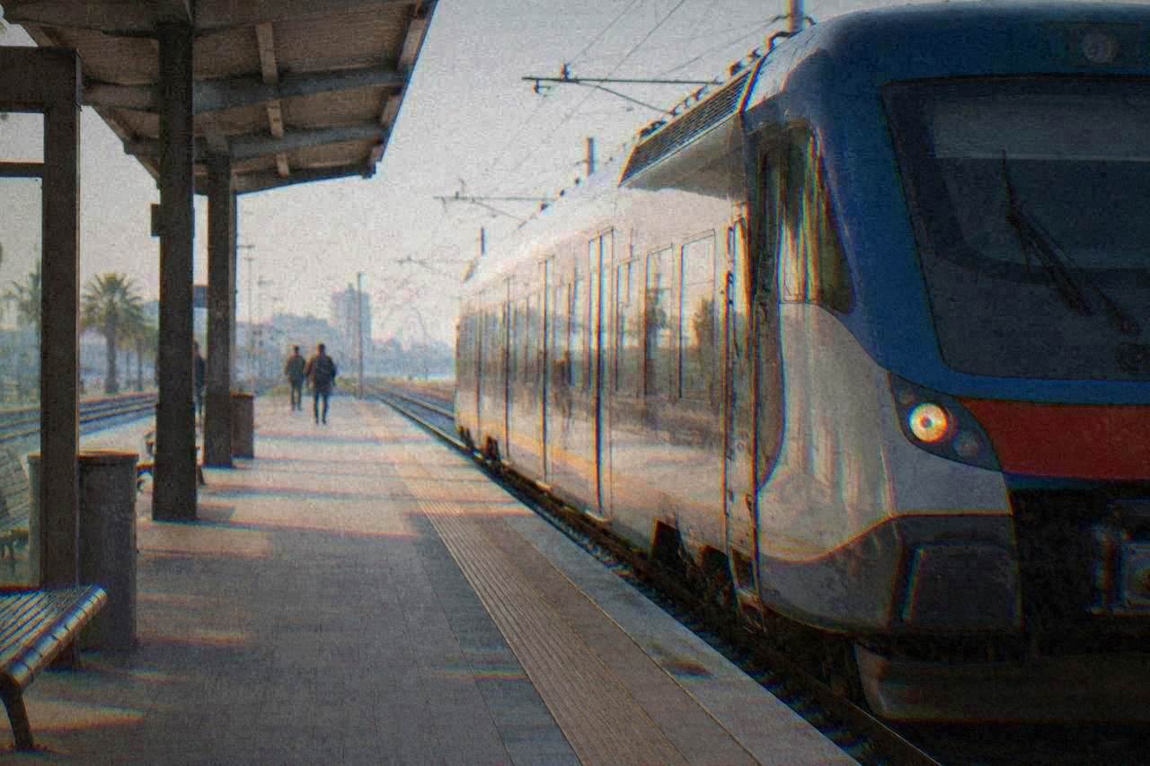 A regional train waiting at a sunny Italian railway station platform