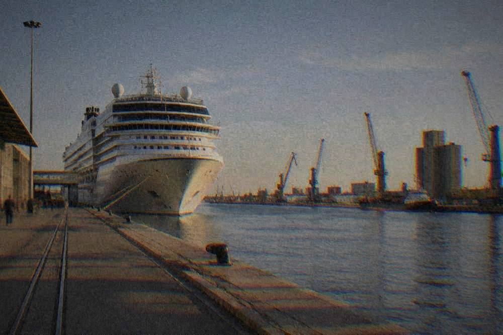 A cruise ship tied up along a canal dock at an industrial port terminal near the Adriatic coast