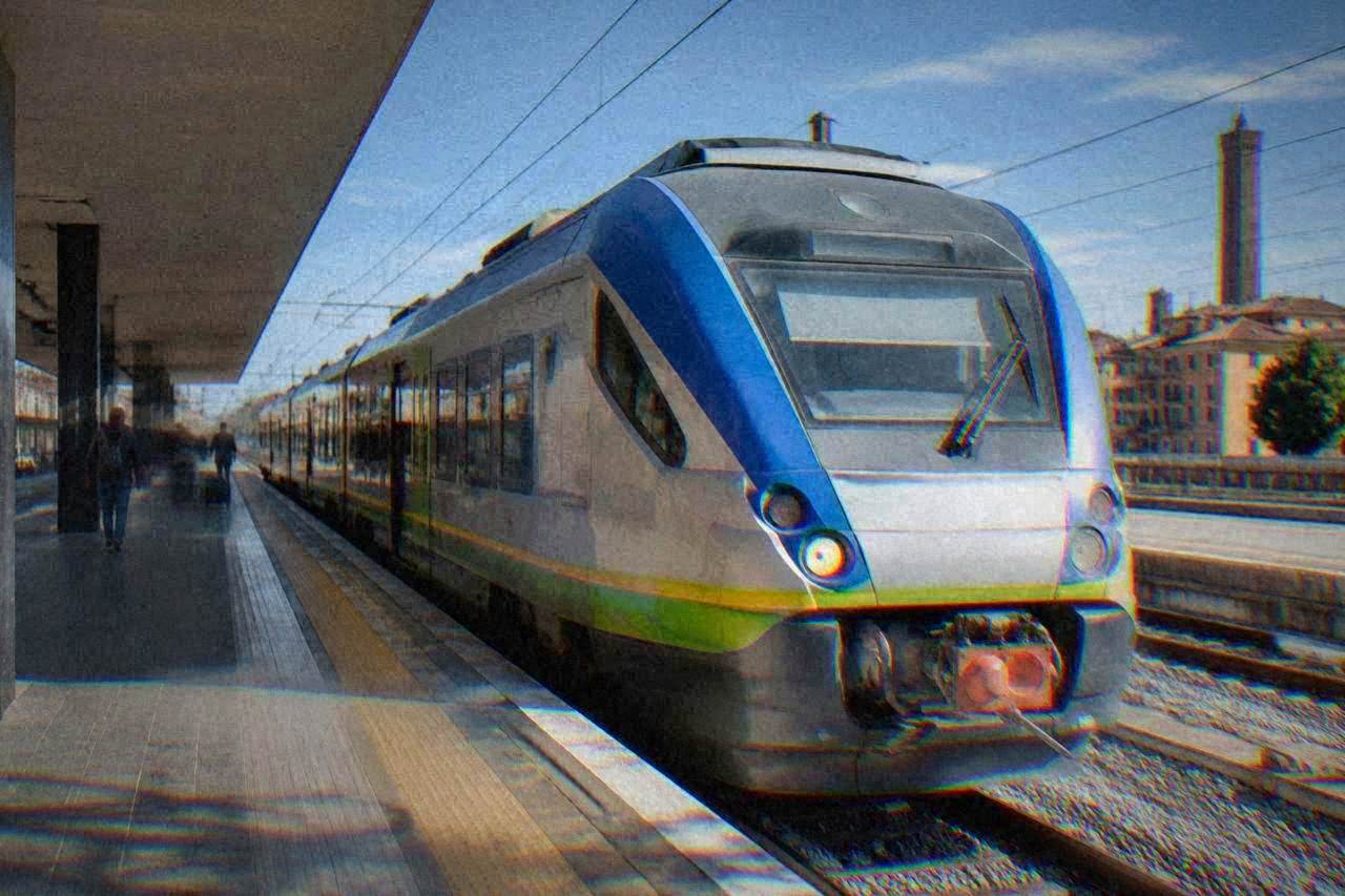 A regional train parked at an Italian railway station platform under a clear sky