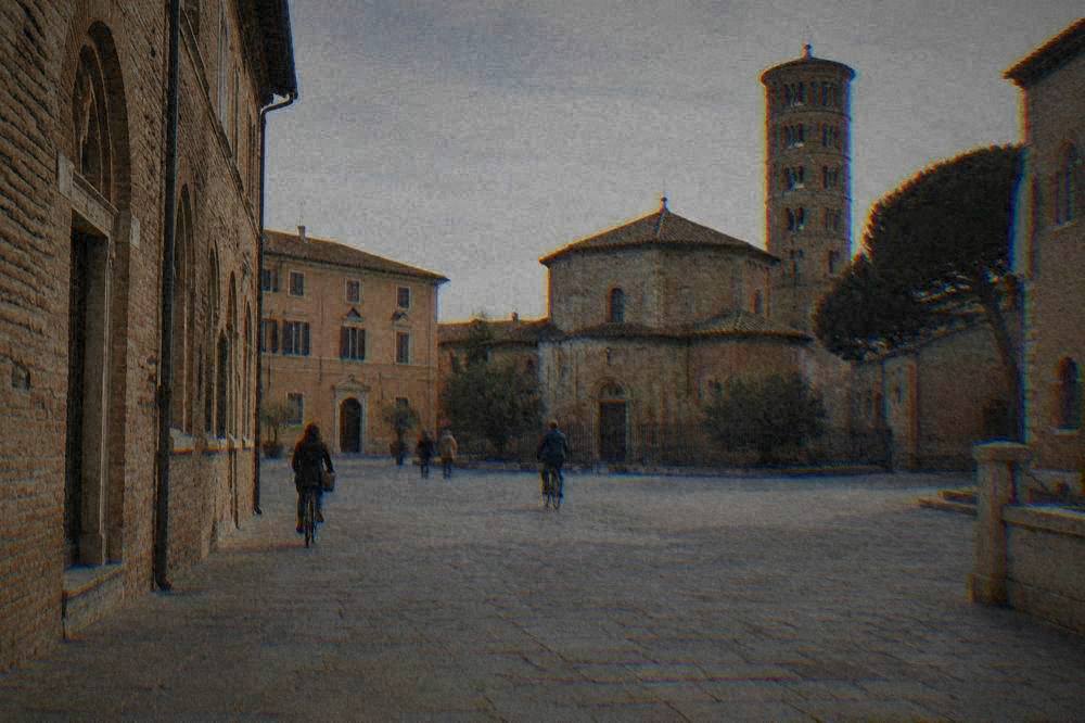 A quiet paved square in Ravenna's historic centre with brick facades and cyclists passing