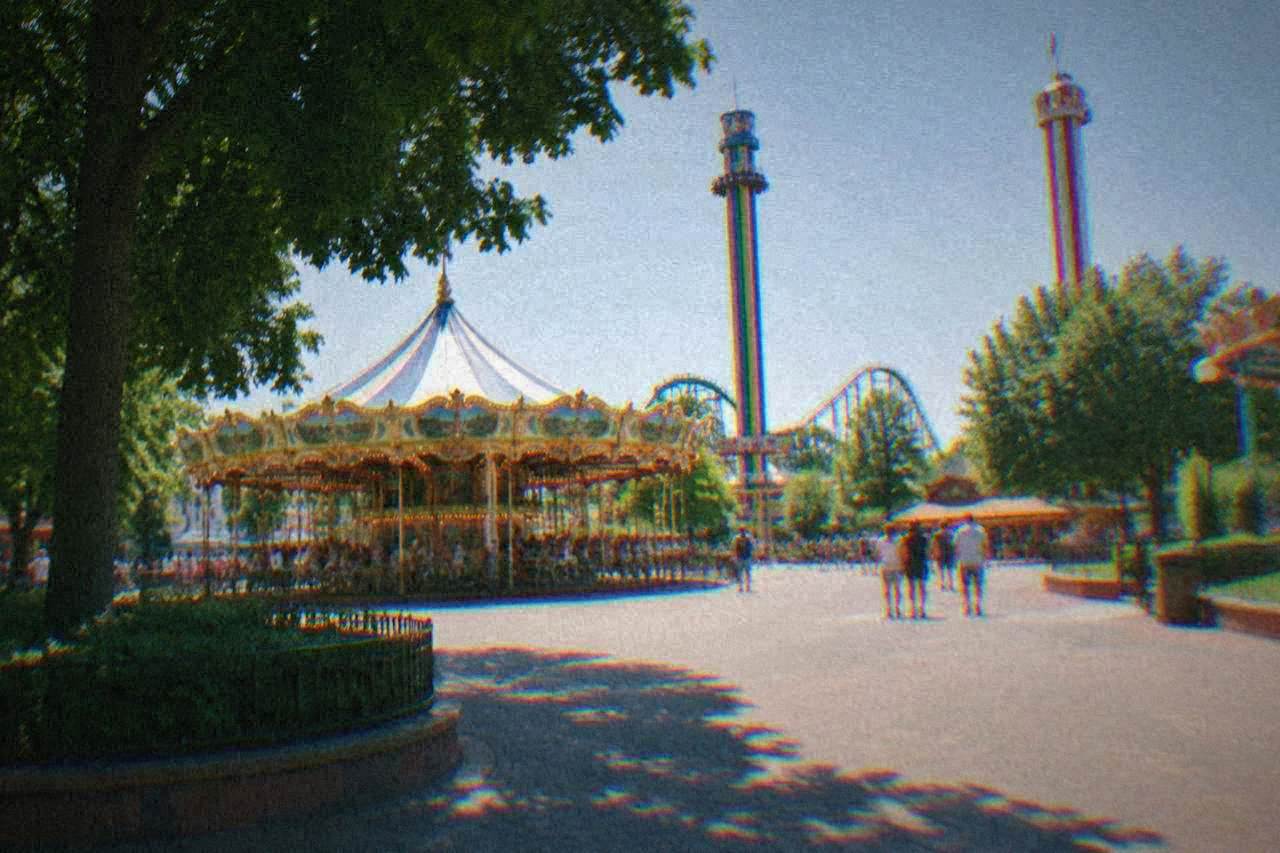 A large amusement park entrance plaza with a carousel and striped ride towers under a clear sky