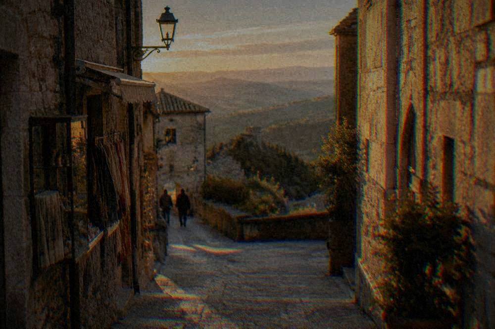 A narrow stone street with shops and a view over the hills from the historic centre