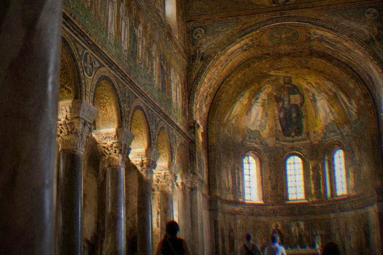 A golden Byzantine mosaic interior with saints and arches lit inside an ancient Ravenna church