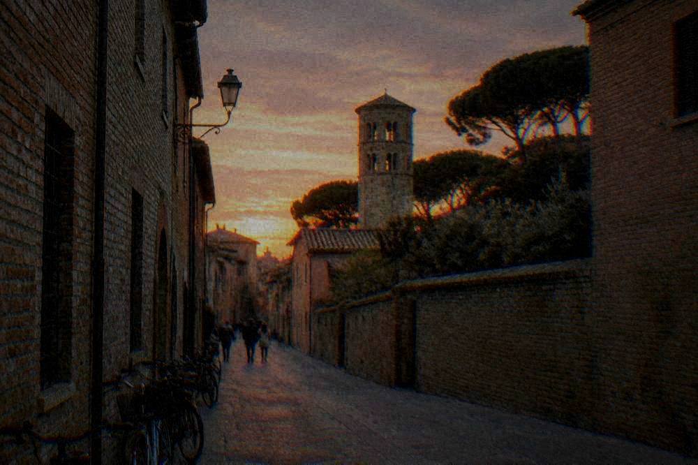A narrow Ravenna street with brick facades, bicycles and a stone tower in soft evening light