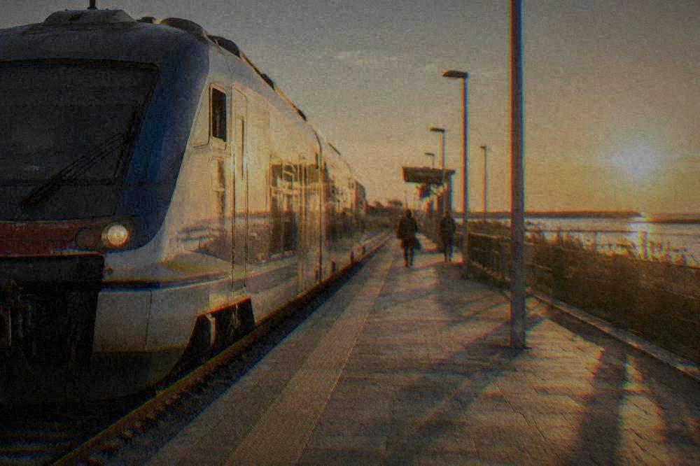 A regional train waiting at an Italian railway station platform beside a sunny platform