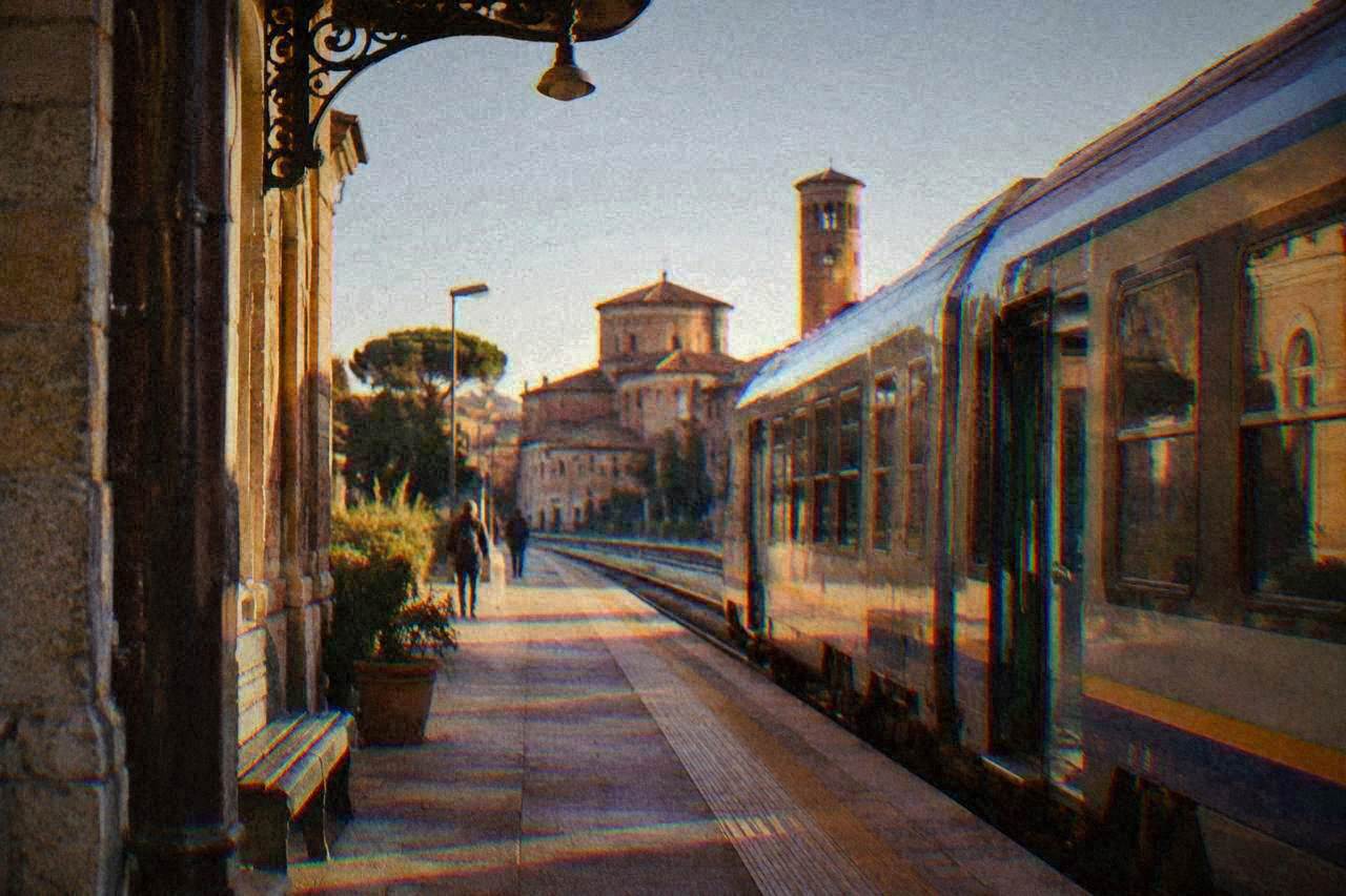 Train waiting at a small Italian railway station platform on a bright morning