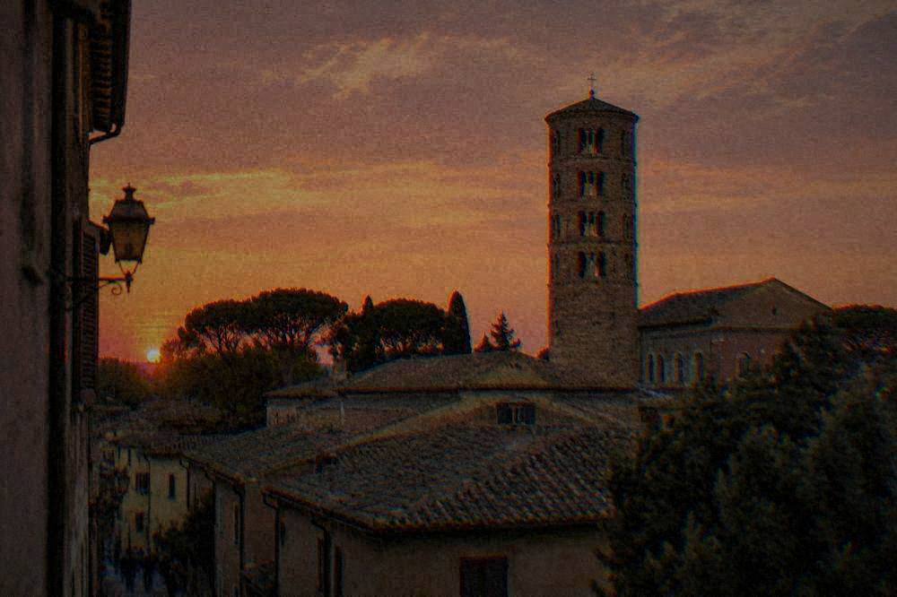 Brick bell tower rising above rooftops in central Ravenna at dusk