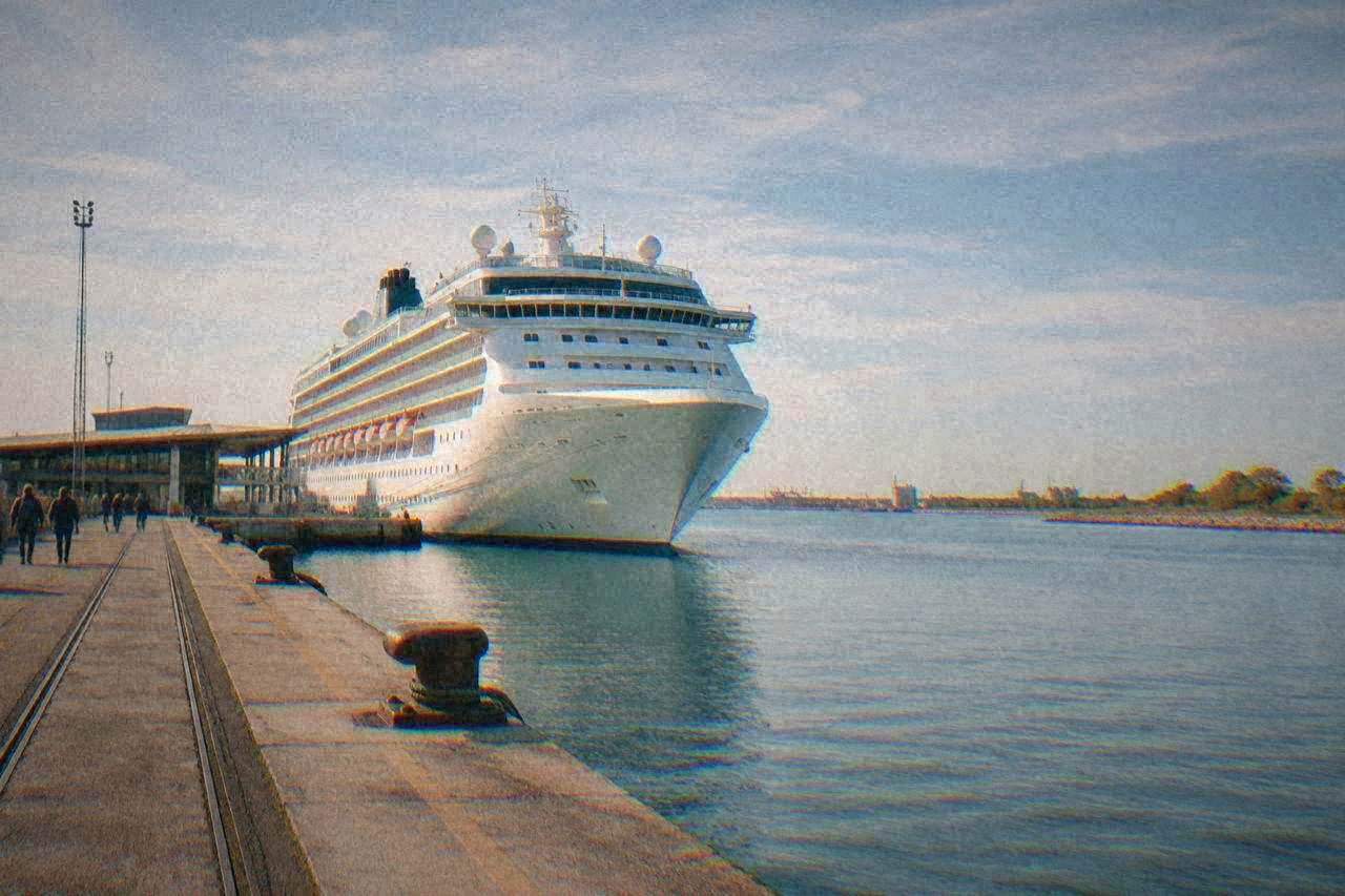 A cruise ship docked at a port terminal beside a calm water channel
