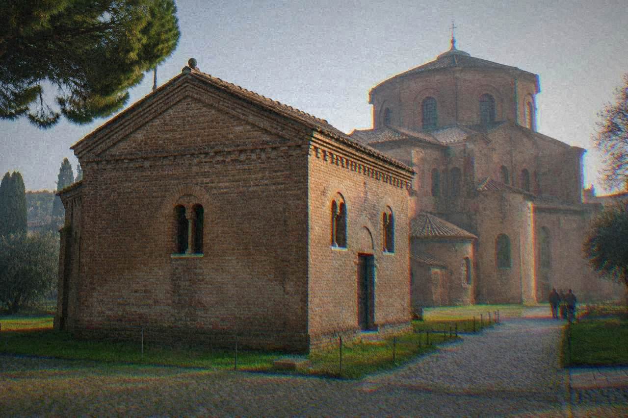 A small brick chapel with a plain tower standing in a quiet courtyard beside a church in Ravenna