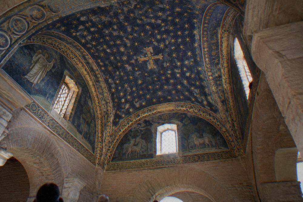 An interior of gold and blue glass mosaics covering a domed ceiling with star patterns and figure scenes