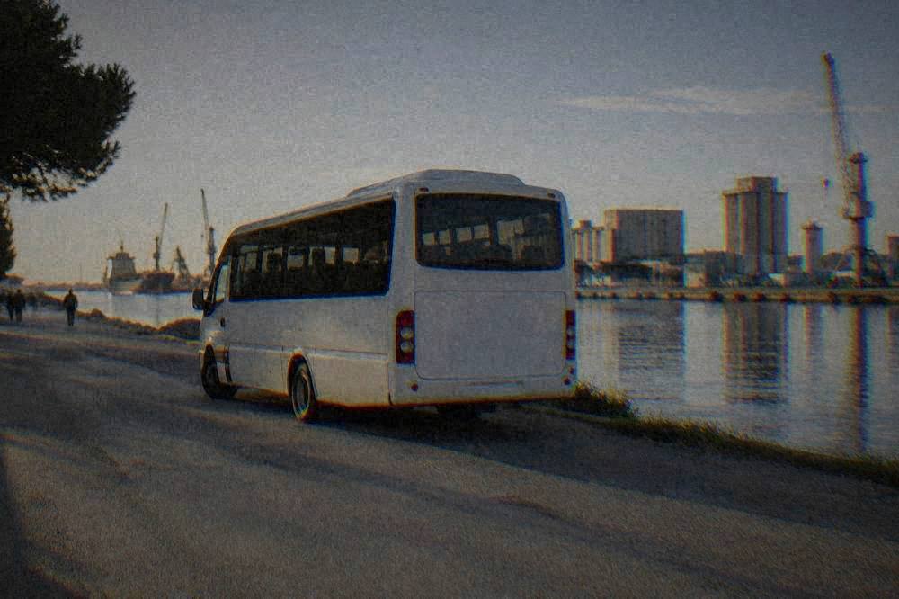 A shuttle bus parked on a quiet road beside a canal and industrial port buildings