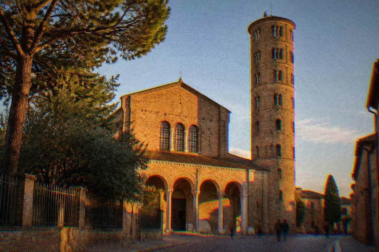 The brick facade and tall round bell tower of a basilica in Ravenna under a clear sky