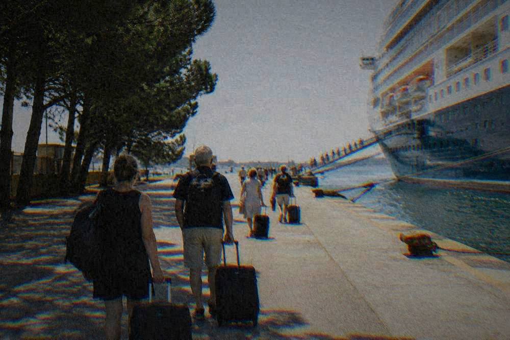 Passengers with suitcases walking along a quay toward a cruise ship gangway