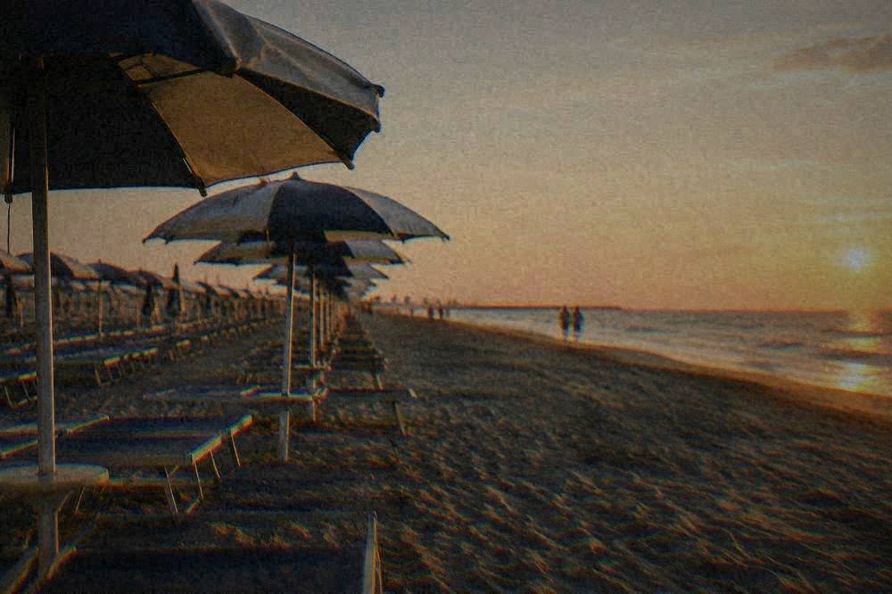 Row of beach umbrellas along a wide sandy Adriatic shoreline in Rimini