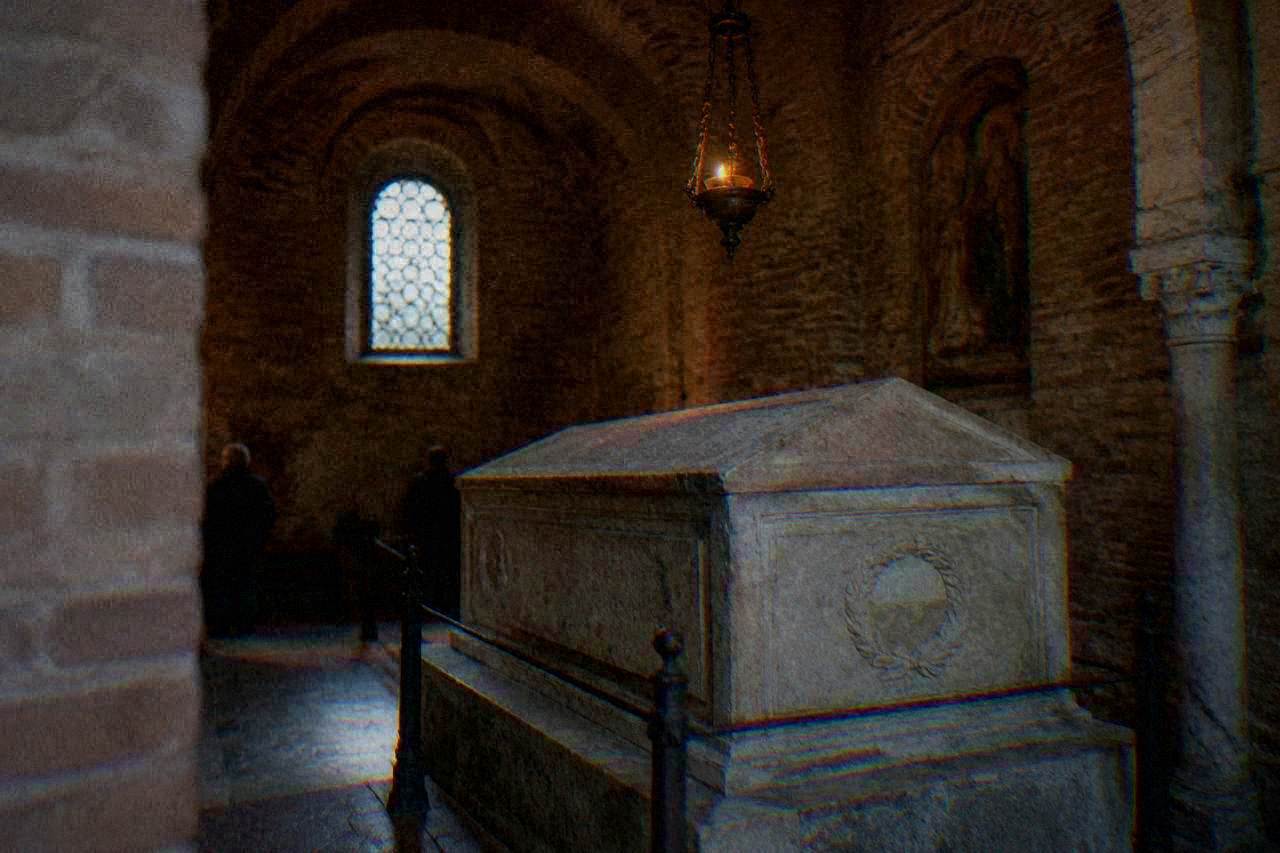 A stone sarcophagus resting in a small brick chapel lit by a hanging oil lamp