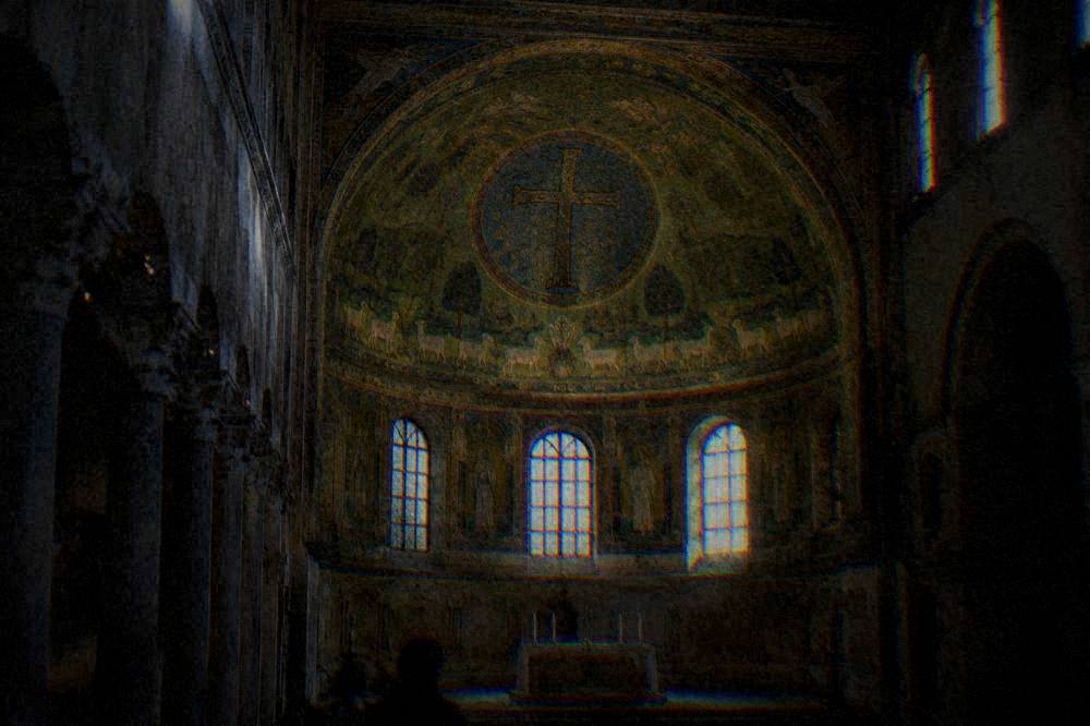 A green mosaic apse with sheep, trees and a jewelled cross inside a dim basilica interior
