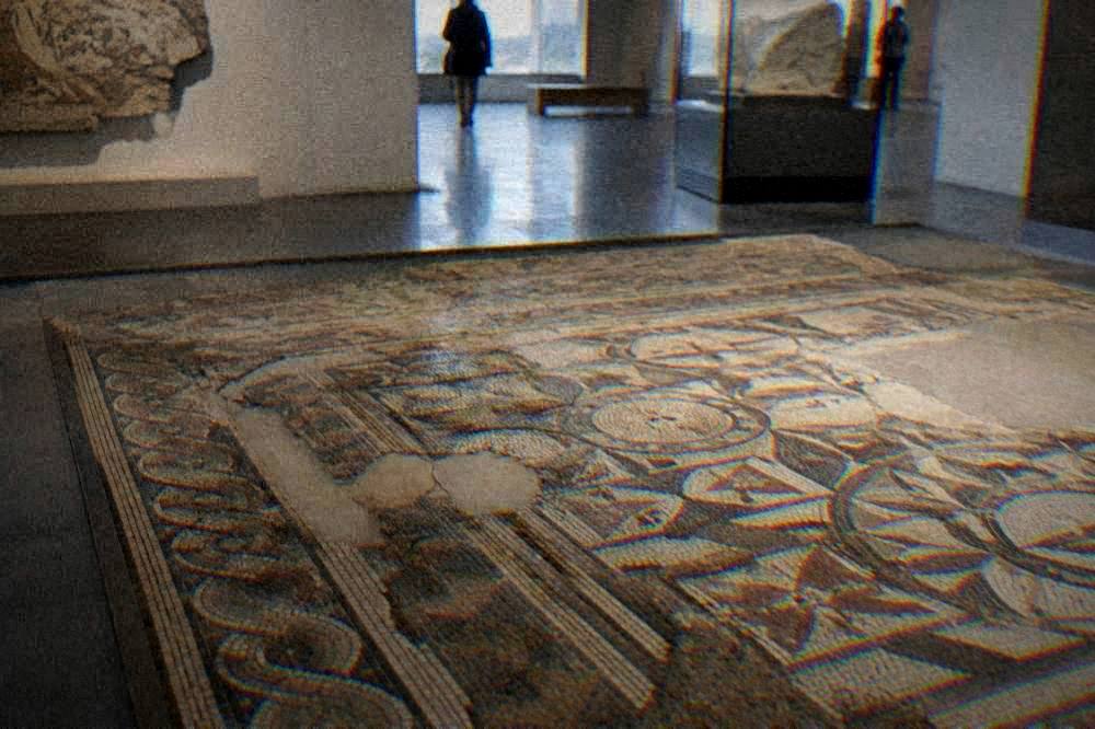 An ancient floor mosaic with geometric patterns displayed inside a museum gallery