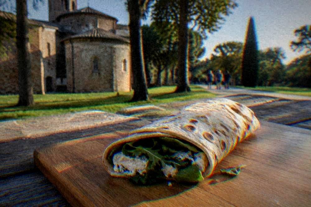 A flat bread rolled around soft cheese and leafy greens on a wooden board