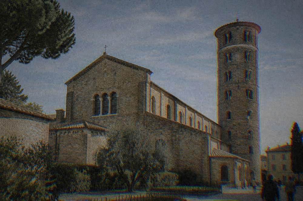 The brick facade and round bell tower of a mosaic basilica in Ravenna under a clear sky