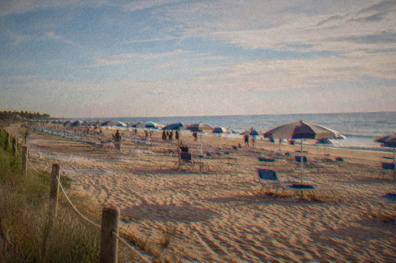 A wide sandy beach with rows of umbrellas and a calm sea under a summer sky