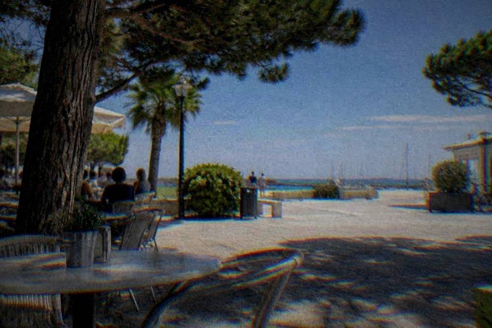 A small square in a seaside resort with cafe tables and pine shade