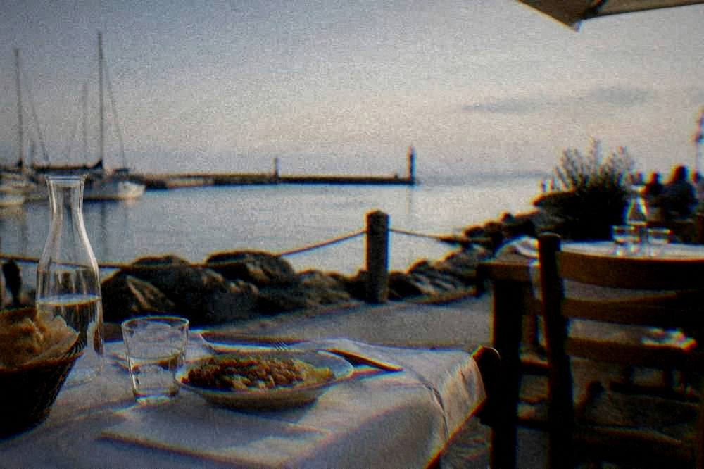 A dinner table outside a small restaurant with paper tablecloth and sea in the background