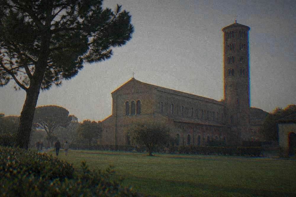 The tall brick bell tower and long brick facade of a basilica seen across a green lawn