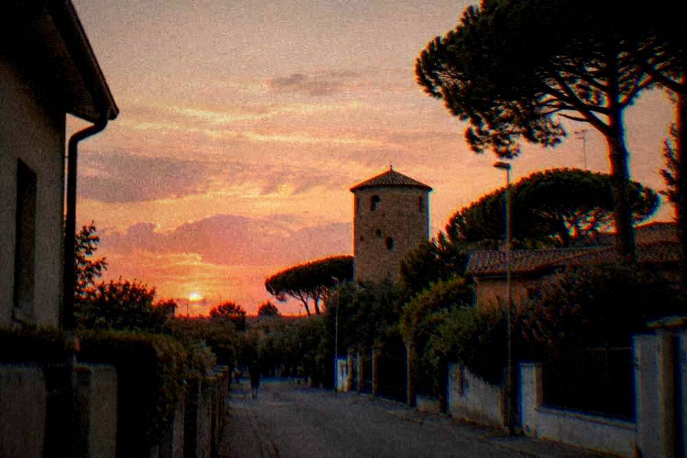 Evening light over rooftops and a round brick tower seen from a quiet street