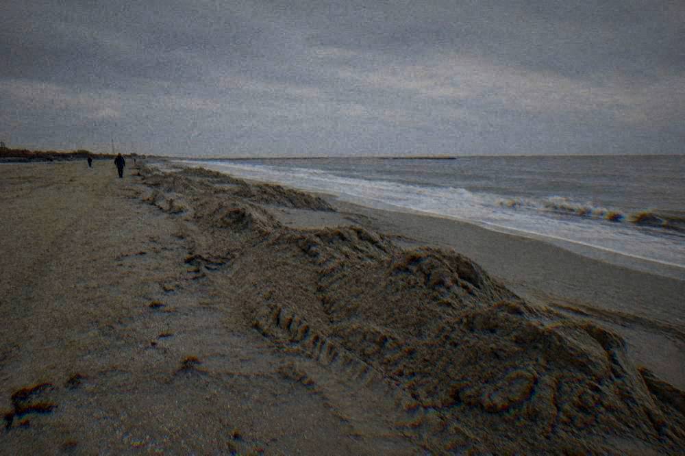 An empty winter beach under a grey sky with mounded sand along the shoreline