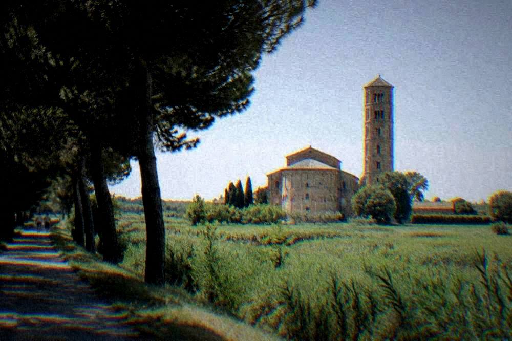 The brick apse and campanile of a basilica rising above flat green countryside