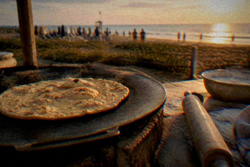A flatbread cooking on a griddle beside a rolling pin and flour
