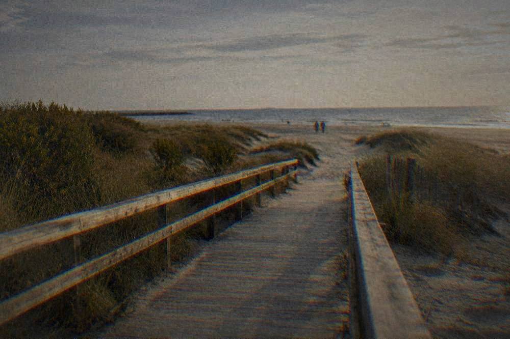 Wooden walkway crossing dunes toward a wide sandy beach in late afternoon light
