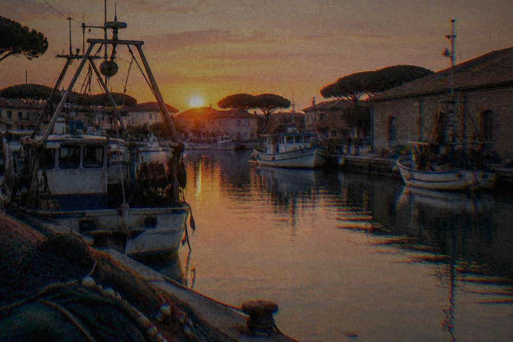 A canal basin with moored fishing boats, nets and brick harbour buildings in soft evening light