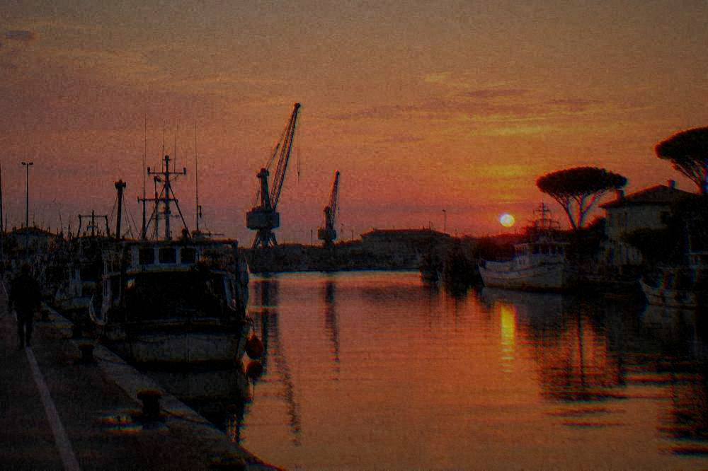 A canal harbour at sunset with silhouetted cranes and calm water reflecting an orange sky
