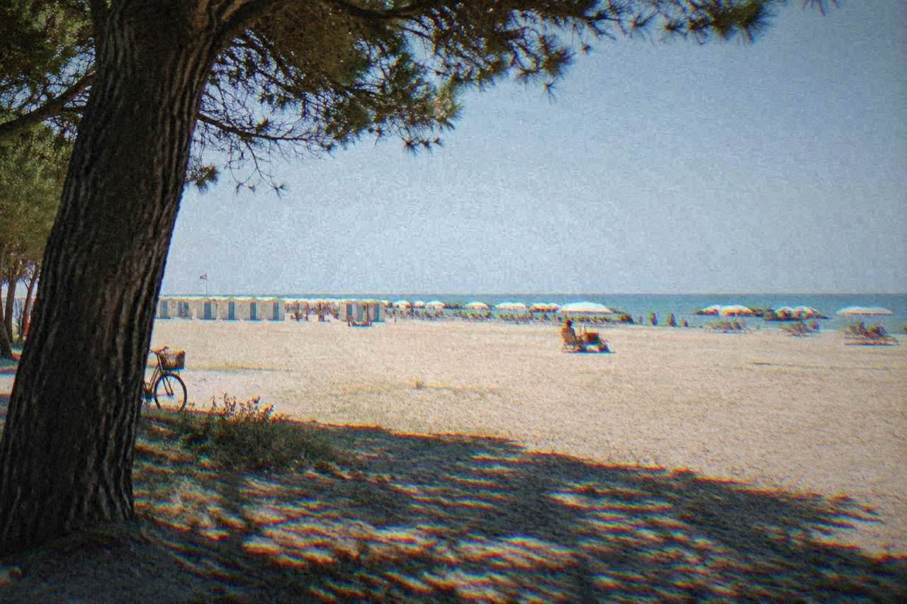 A wide sandy Adriatic beach with a line of parasols and beach cabins behind it under a clear sky