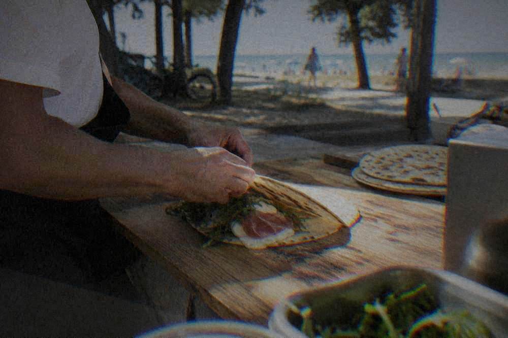 A piadina flatbread being folded around filling on a wooden counter