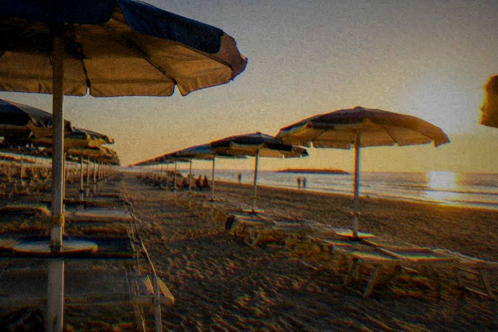 Rows of beach umbrellas on sand under a hot midday sun
