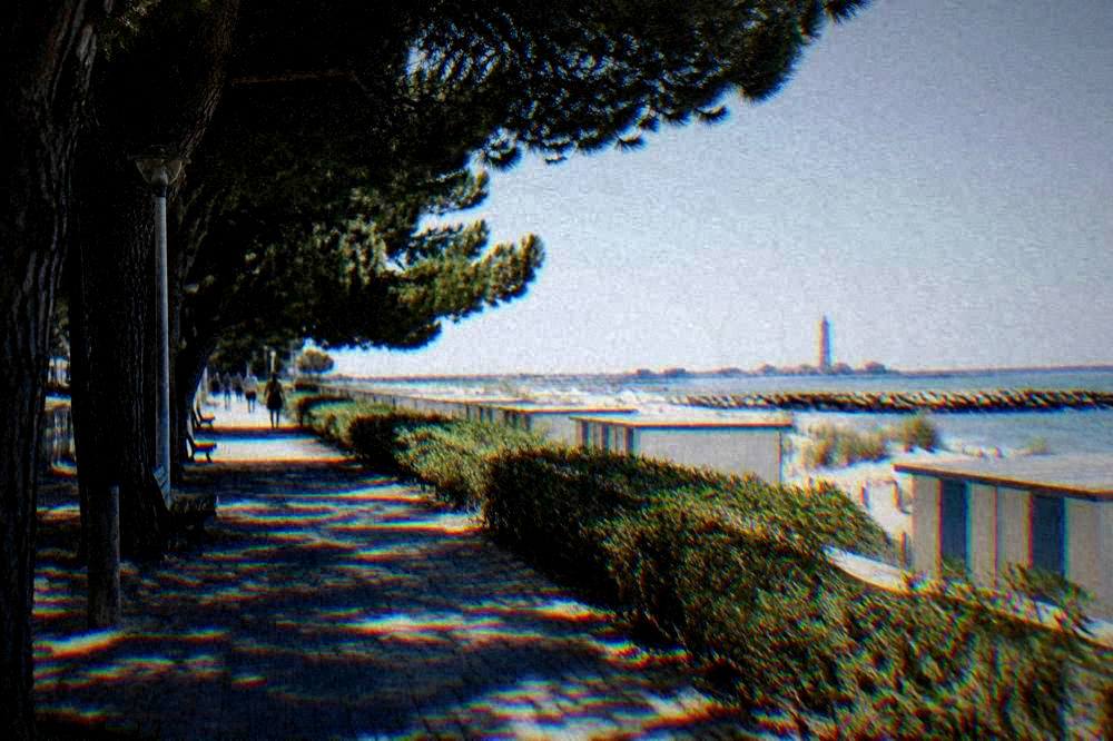 A quiet seaside promenade with low beach cabins and a distant lighthouse