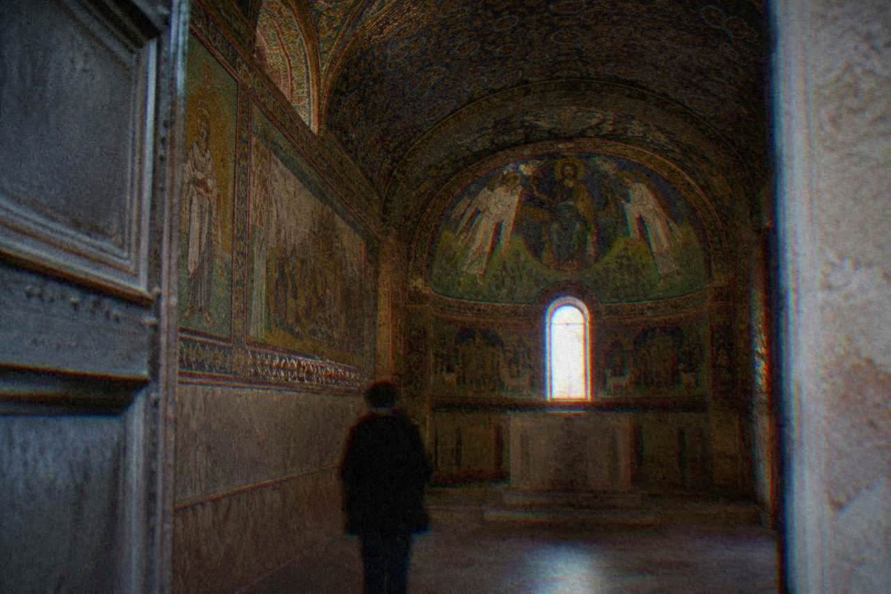 A small vaulted chapel interior with mosaic decoration lit softly through a doorway