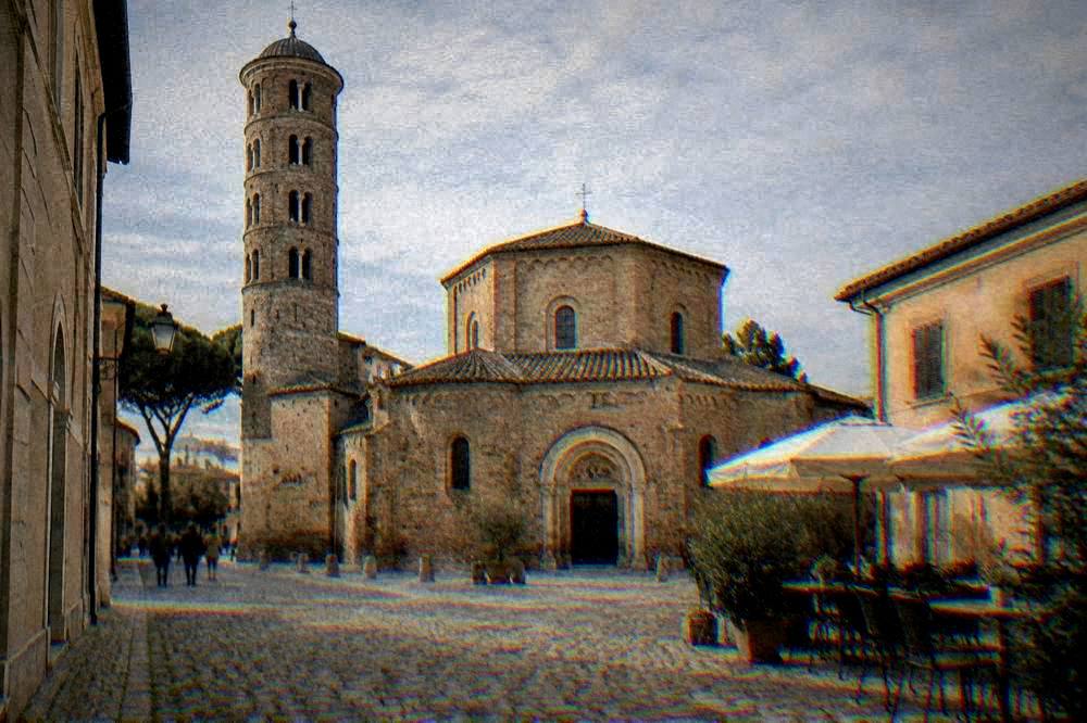 A cobblestone piazza with a bell tower and cafe tables in an Italian town