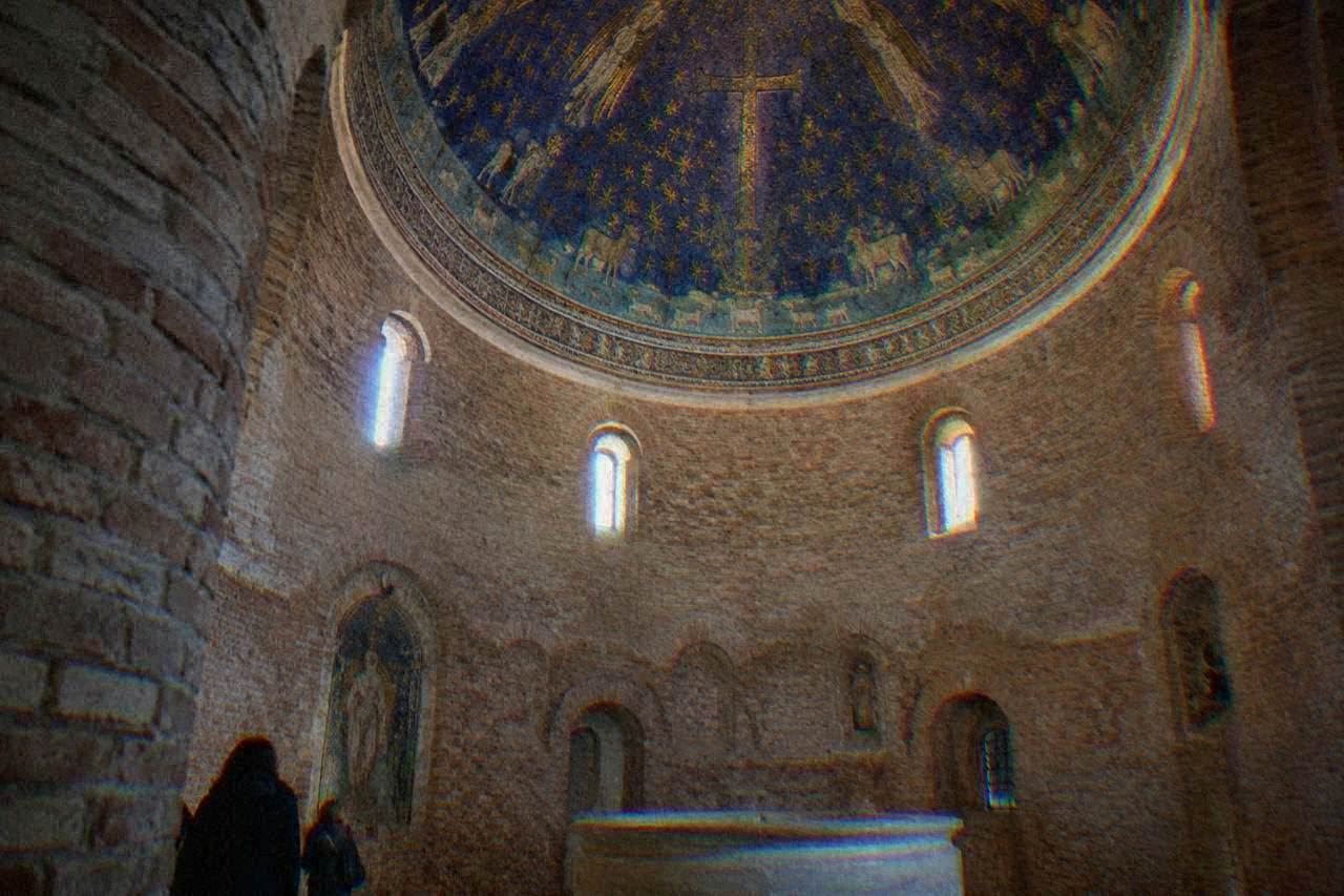 Small brick baptistery interior in Ravenna with a domed ceiling of blue and gold mosaic