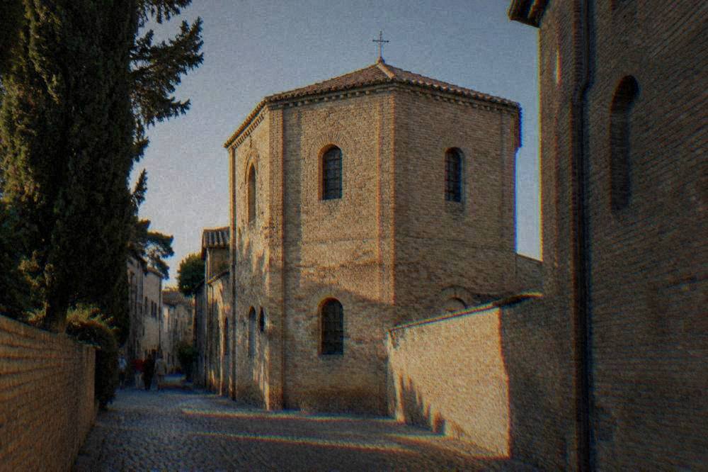 Exterior of the Arian Baptistery showing plain brick walls on a narrow street in Ravenna