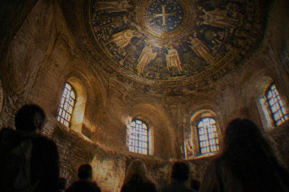 Tourists standing in a small domed interior looking up at a ceiling mosaic