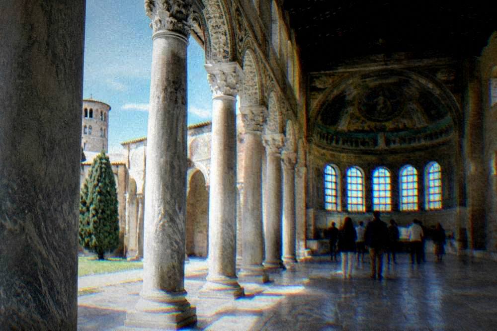 A guide speaking to a small group of visitors standing among columns inside a basilica