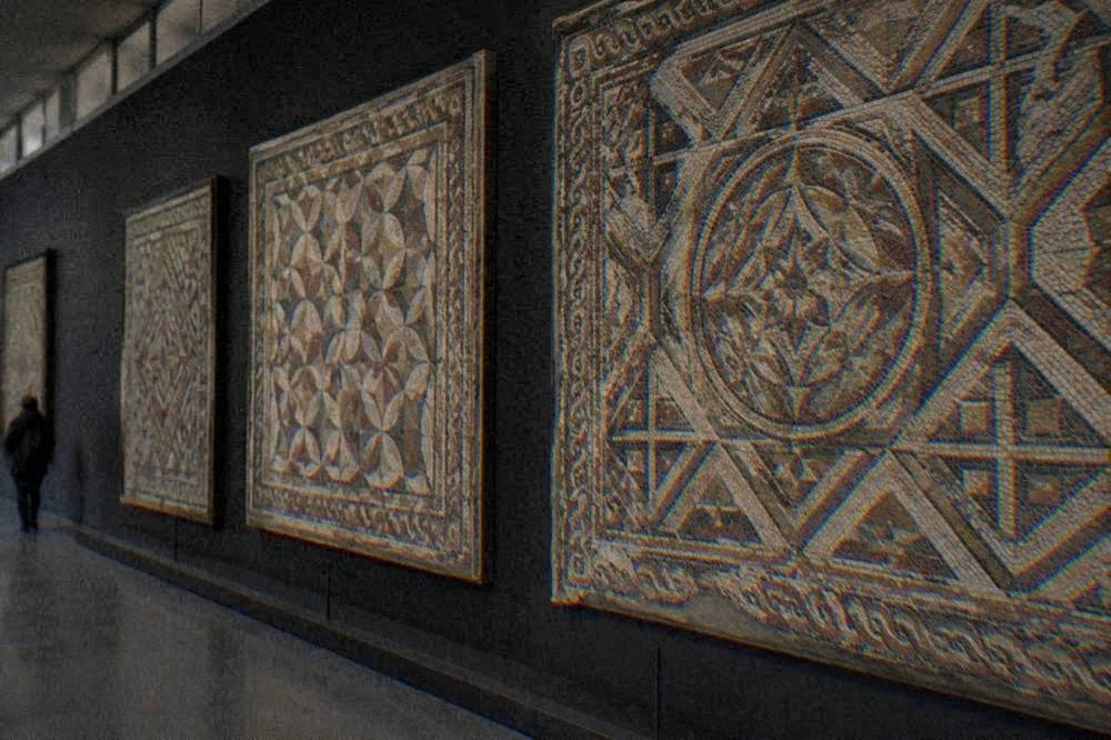 Ancient mosaic panels with geometric patterns displayed on a dark wall in a museum gallery