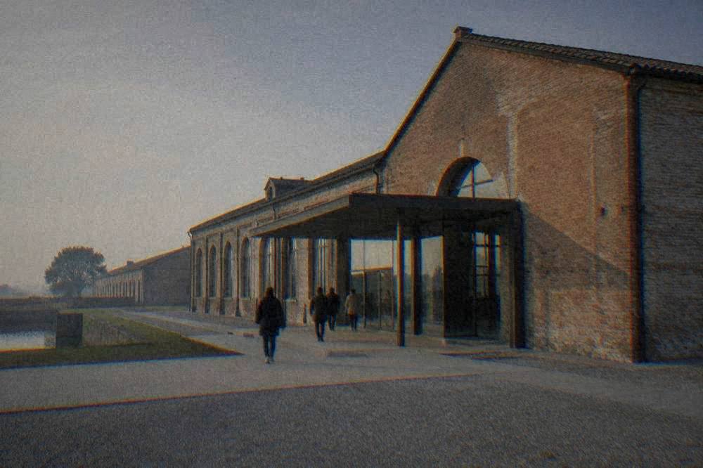 A wide brick factory facade with a museum entrance canopy and a few visitors walking toward it