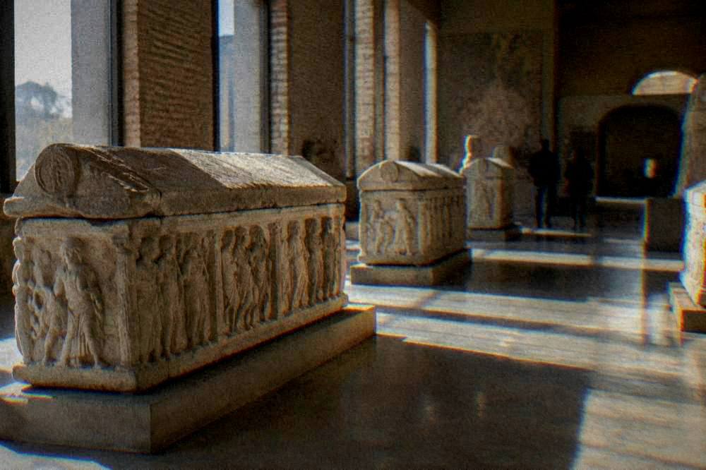 Sunlight falling across a museum hall floor with stone sarcophagi displayed in a row